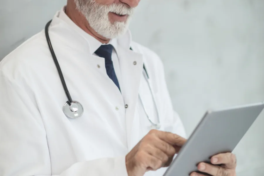 A doctor in a white coat reading notes on a tablet computer