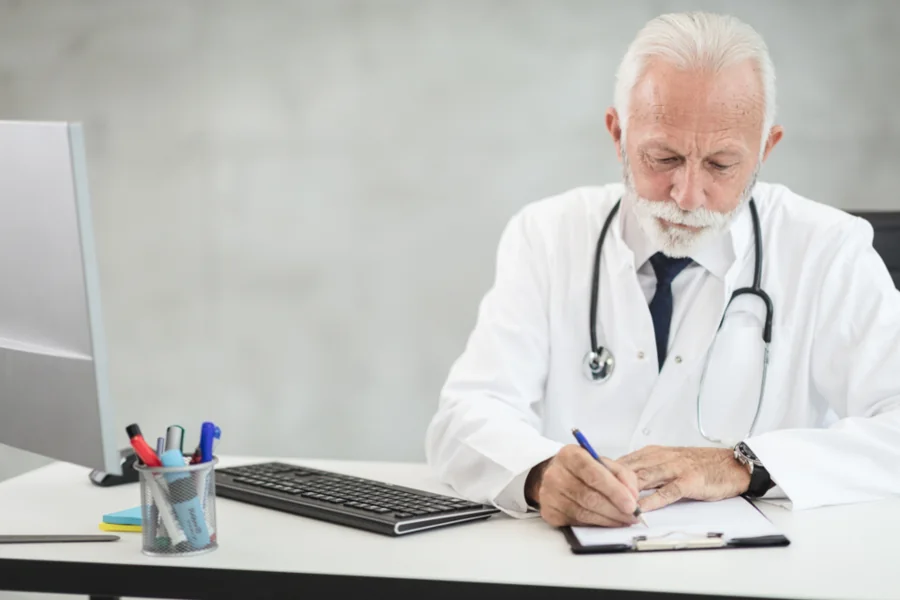 A doctor writing at a desk in a consulting room