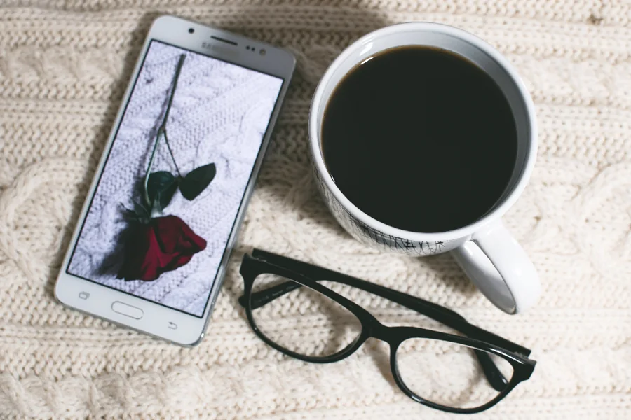 A smartphone, reading glasses and a cup of coffee on a knitted blanket